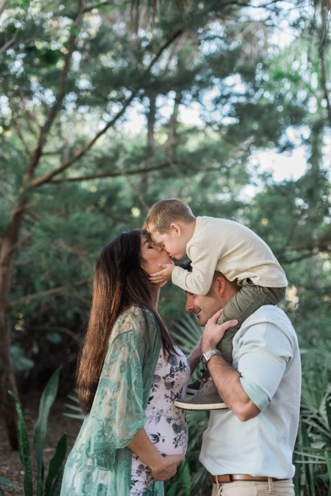 Little boy on dad's shoulders kissing mom