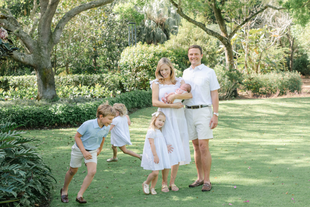 Mom looking down at daughter, holding other daughter while other kids run around