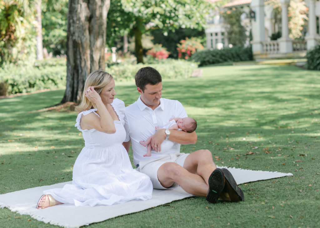 Mom and dad looking at baby, sitting on a blanket