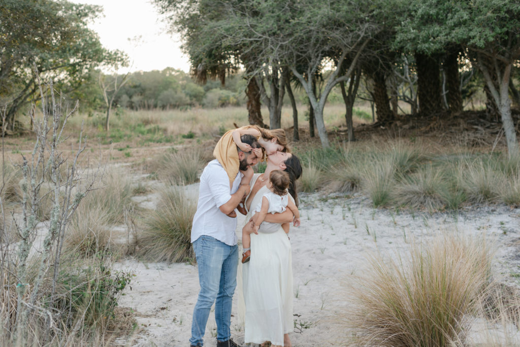 Older daughter on dad's shoulders, kissing mom holding baby