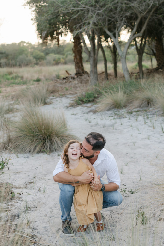 Dad crouched down kissing daughter on cheek