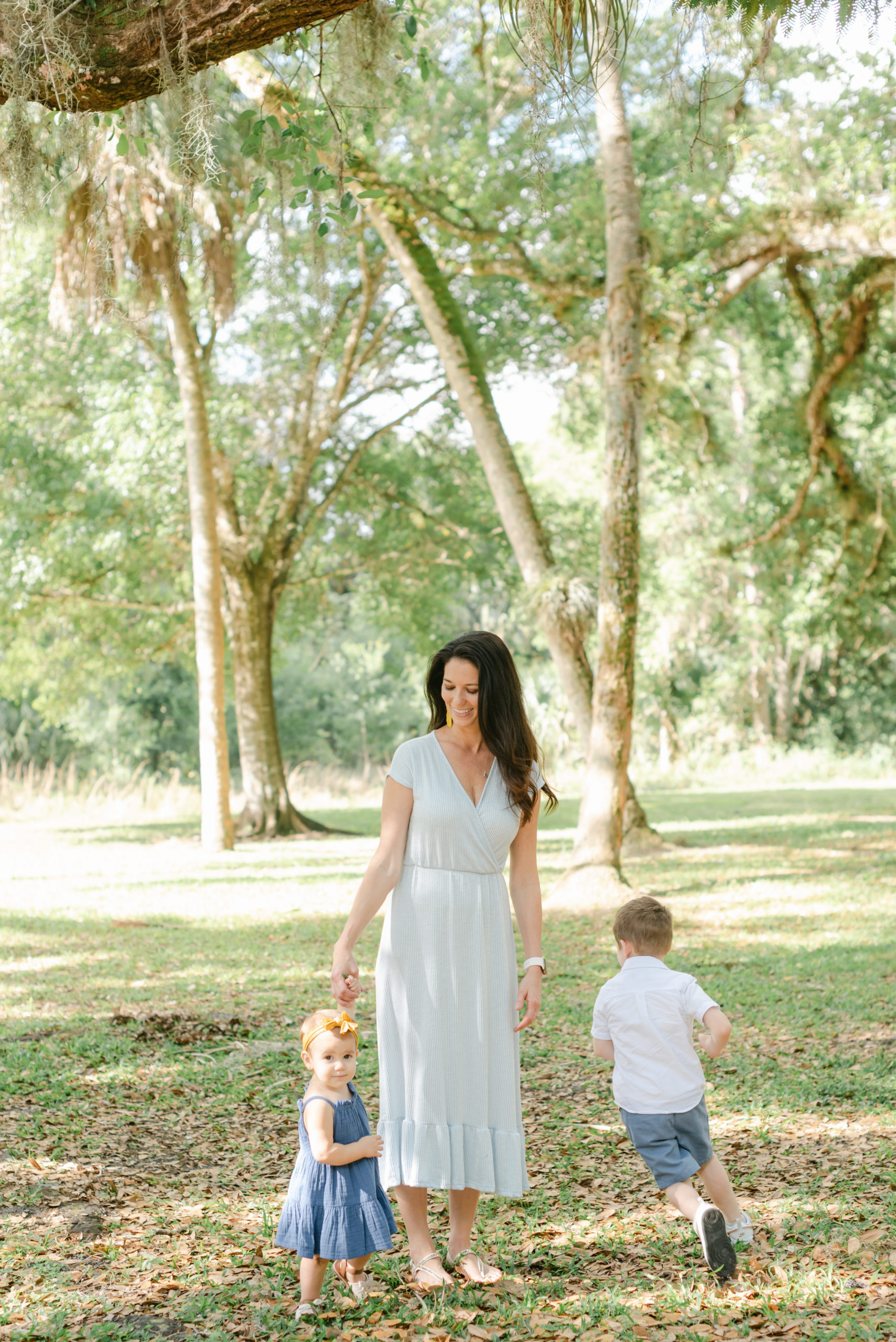 Mom holding daughter's hand while son runs around