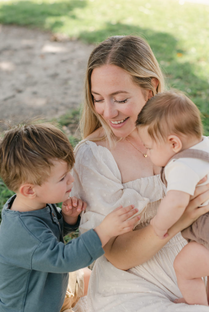 Mom smiling looking at toddler, holding baby