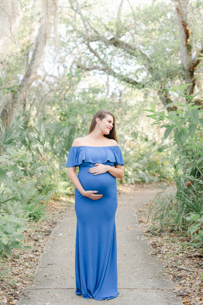 Mom to be holding belly looking away in a blue dress