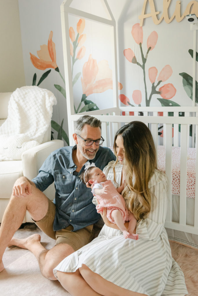 Mom and dad looking at baby sitting in front of crib