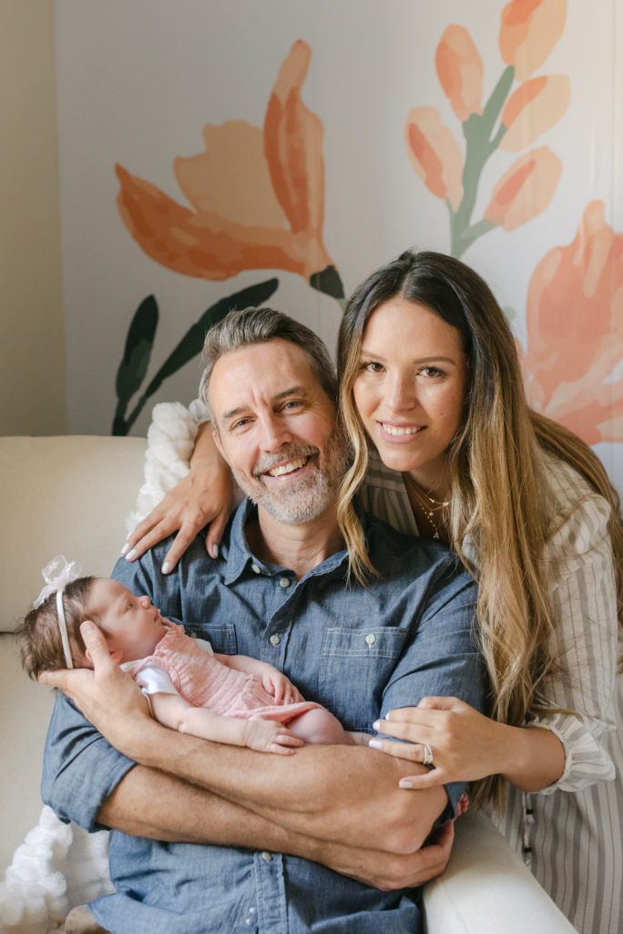 Dad sitting in chair holding baby, mom crouched down behind smiling