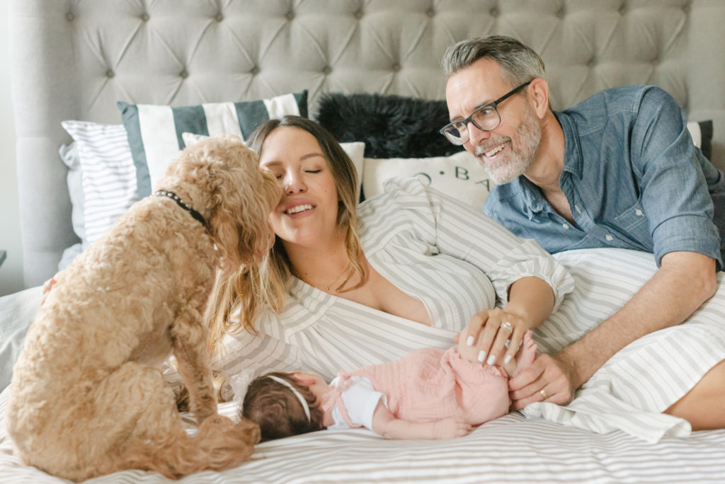 Mom laying down, dog kissing mom, dad looking at mom