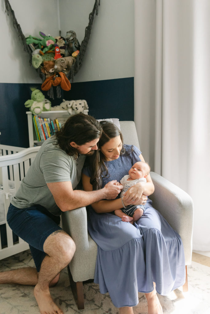 Mom and dad by rocker holding baby's hand