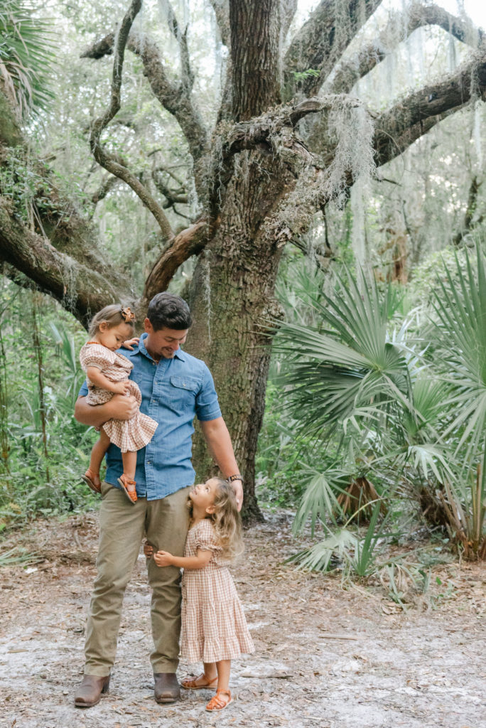 Dad holding younger daughter looking down at older daughter 