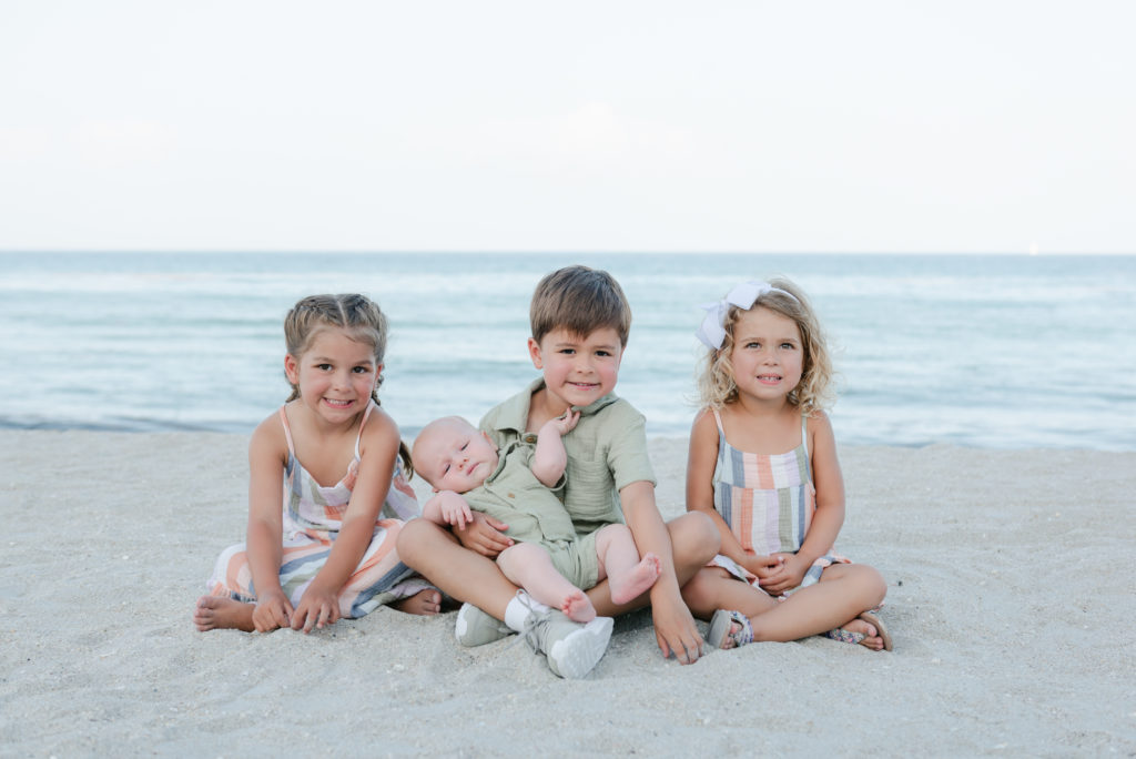 Two girl and two boy cousins sitting on the sand at the beach by Palm Beach family photographer