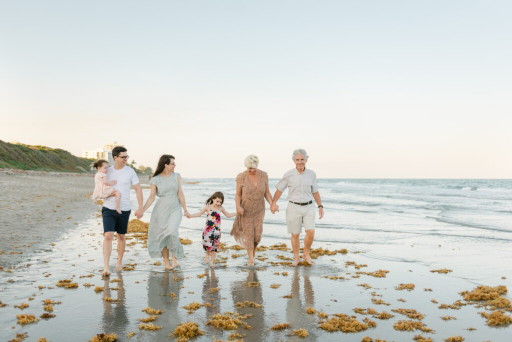 Family including grandparents walking hand in hand down the beach